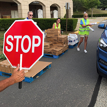 A red stop sign is on the left with volunteers handing food to someone in their car at a Mobile Pantry