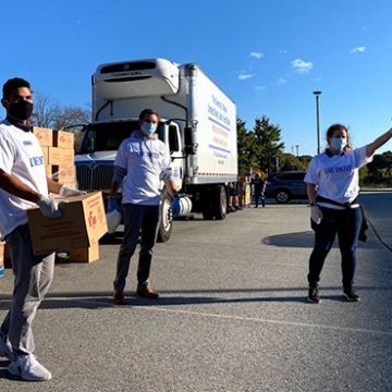 Three volunteers holding food boxes and directing traffic flow at a Mobile Pantry distribution