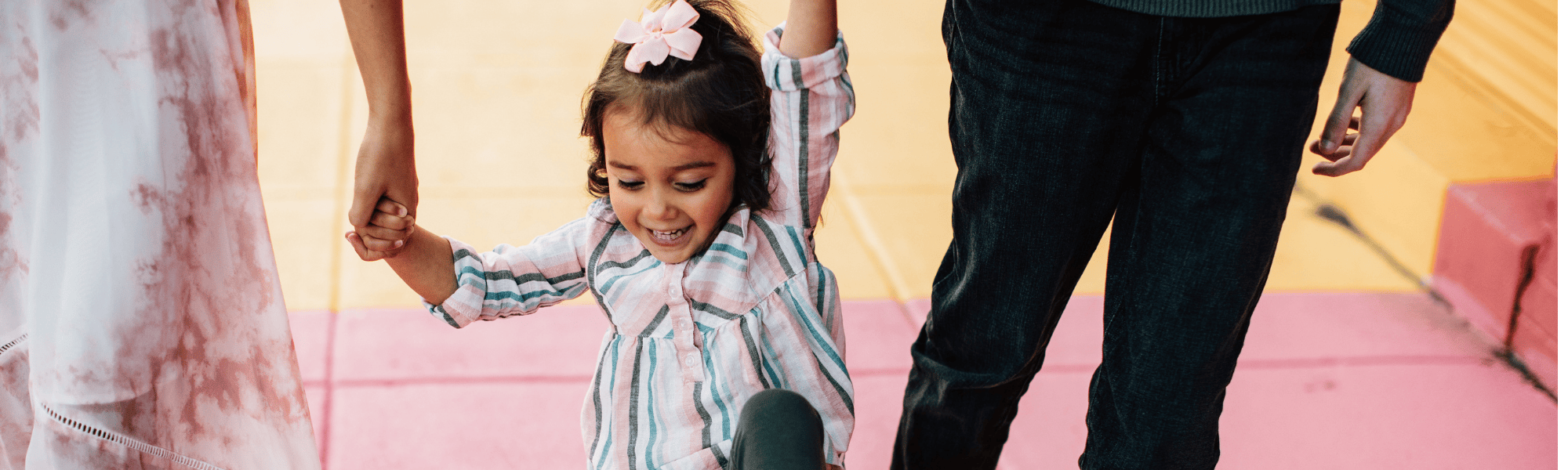 Young child holding the hands of its parents