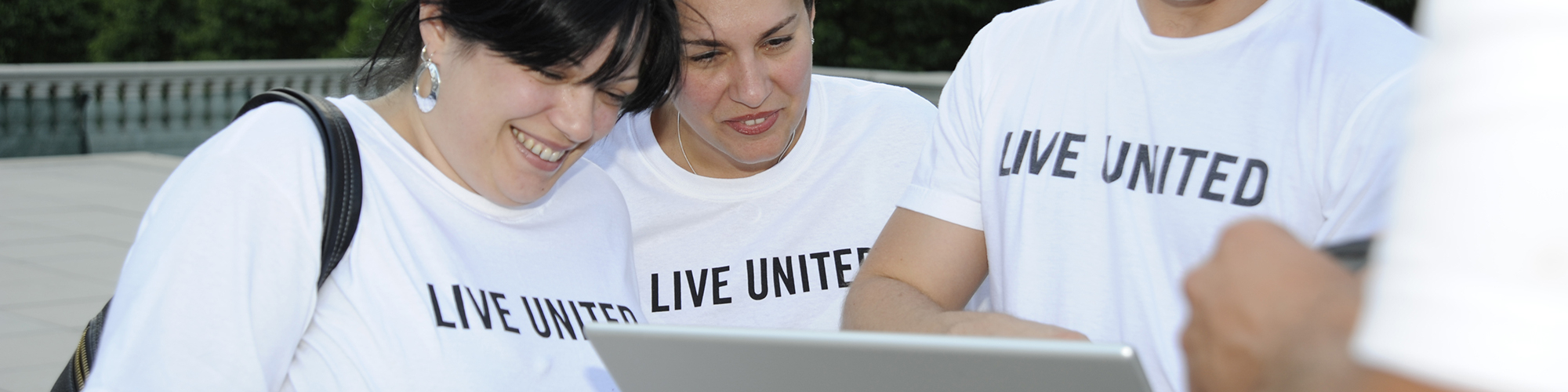Three people in white Live United tshirts looking at a computertablet