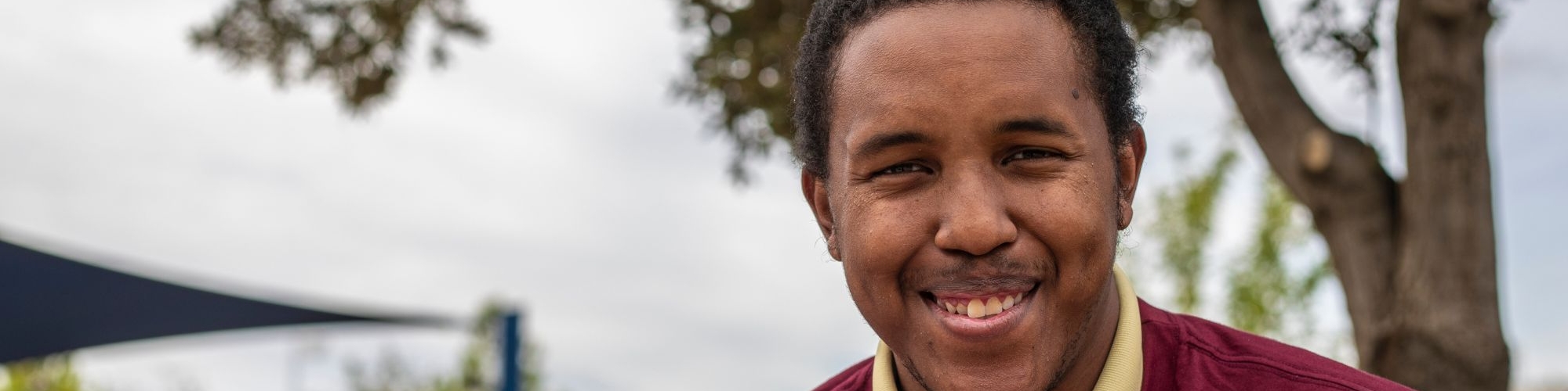 A young man smiling at the camera in a natural setting